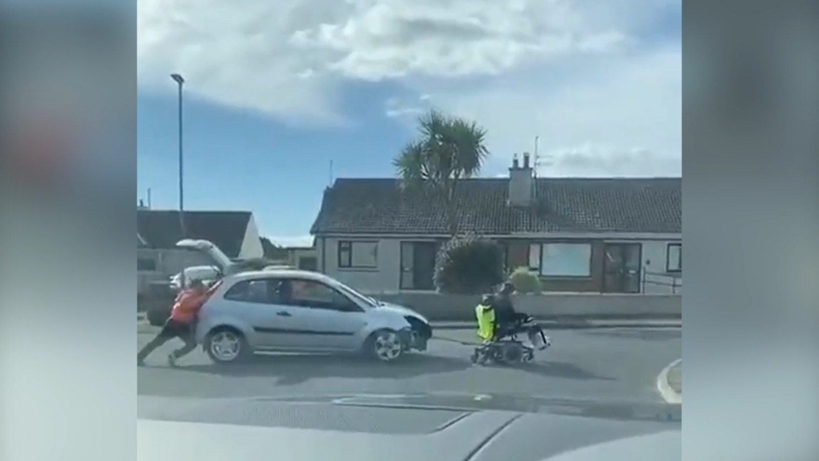 Dos personas tratan de remolcar un coche con una silla de ruedas motorizada.