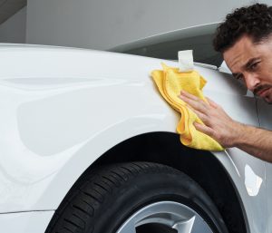Un hombre limpia el exterior de su coche con un paño de microfibra.