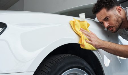 Un hombre limpia el exterior de su coche con un paño de microfibra.